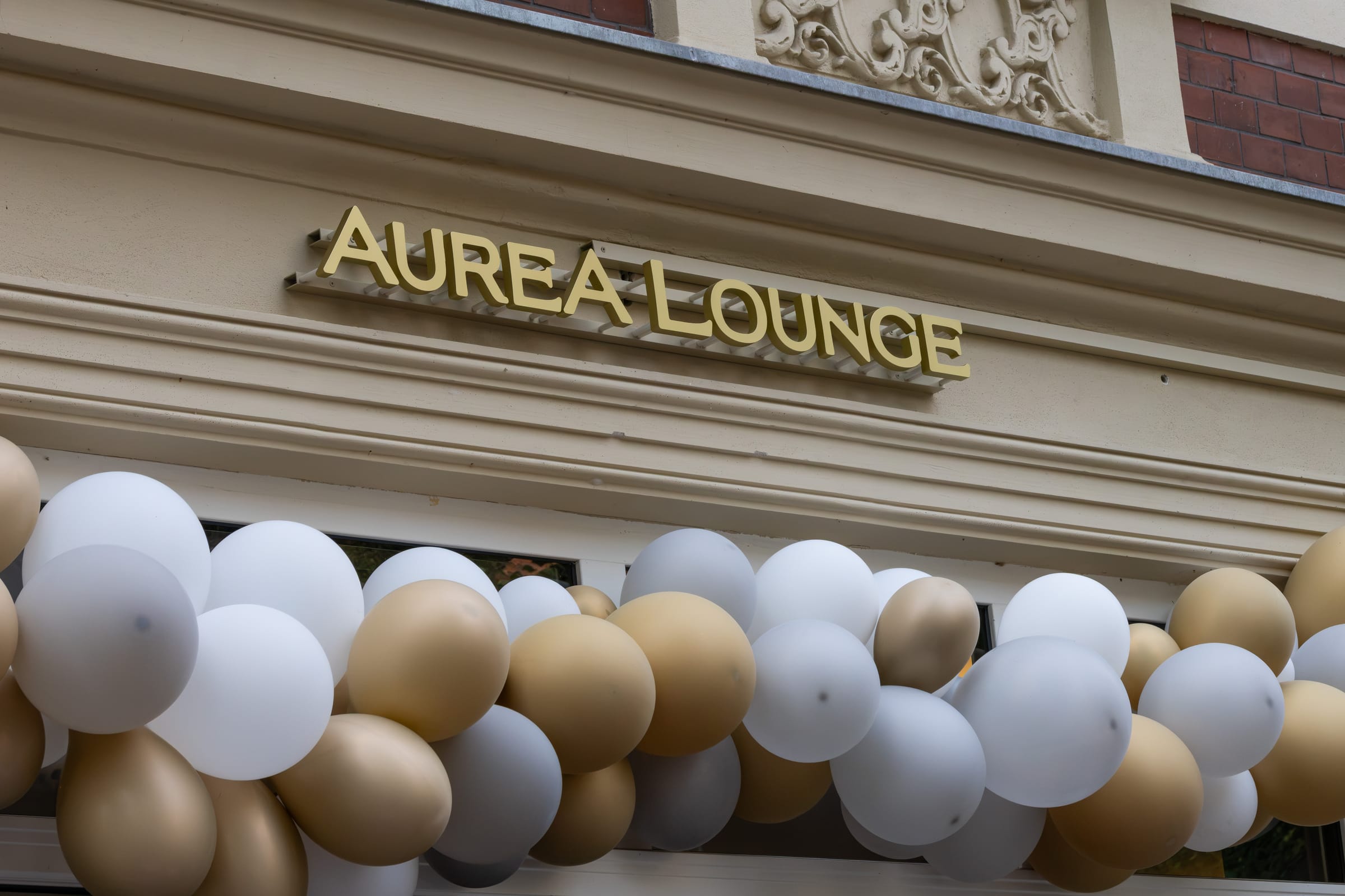 Golden Auréa Lounge lettering on the facade, with white and gold balloons below
