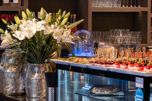 The bar at Auréa Lounge: white lilies and finger food on the counter, glasses on the shelves behind