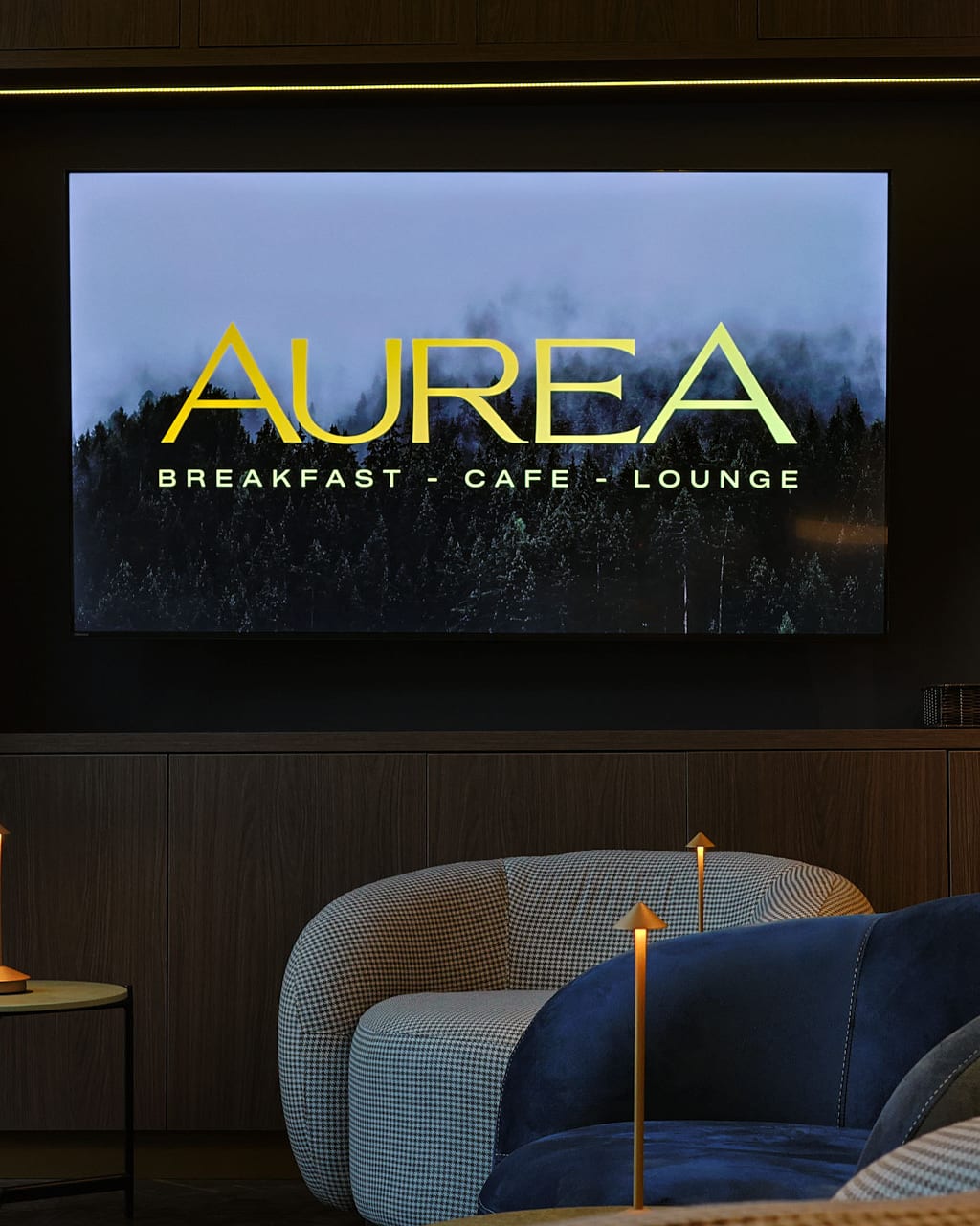 The lounge at Auréa: the Auréa screen above velvet and houndstooth armchairs with golden table lamps